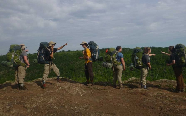 a group of students wearing backpacks stand on an overlook pointing in different directions